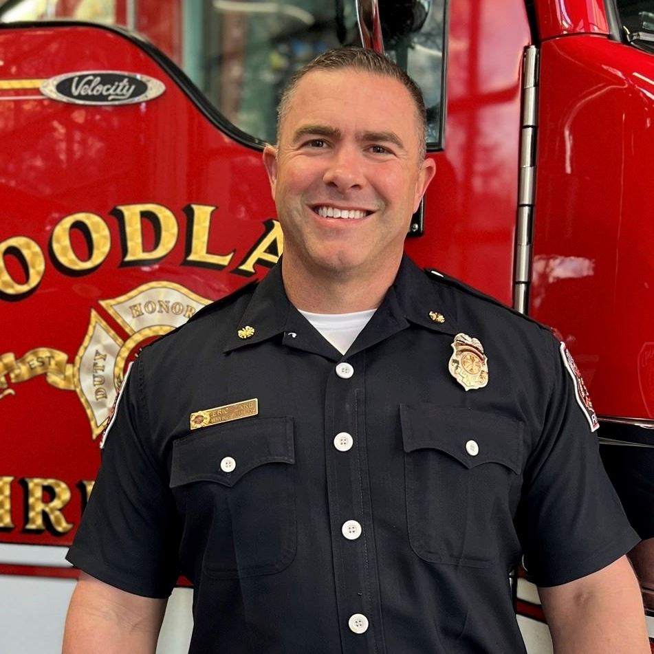Uniformed Woodland Fire Department Chief Zane standing in front of a red fire engine.