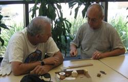 Two men sitting at table with art tools