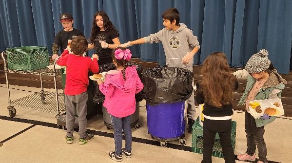 Students line up to sort their cafeteria waste at a school waste sorting station.